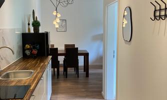 A modern kitchen with a wooden countertop and stylish lamps. In the background, there is a dining area with a table and chairs.