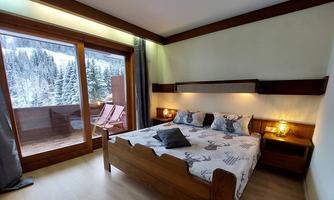 A cozy bedroom with a large bed and wooden details. Through the window, you can see a snow-covered landscape with trees.