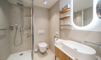 A modern bathroom with a shower cubicle and a sink. The walls are painted in neutral colors, and there are wooden shelves for storage.