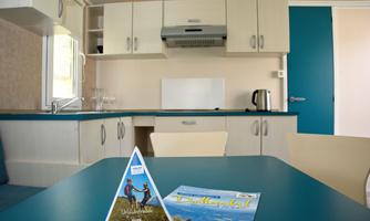 A modern kitchen with a blue table and light cabinets. In the foreground, there are two brochures about vacation offers.