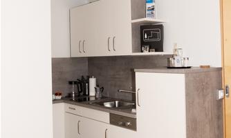 A modern kitchenette with white cabinets and gray countertops. It is compact and well-equipped with kitchen utensils.