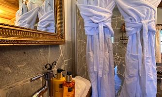 An elegant bathroom with two white bathrobes and a stylish washbasin. In the background, the surroundings are reflected in the mirror.