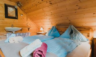 A cozy bedroom with wooden paneling and a double bed. Fresh towels are ready, and a small washbasin is visible.