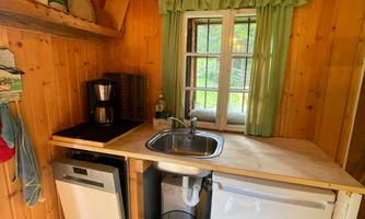 A cozy wooden kitchen with a sink, cooktops, and a refrigerator. The windows are adorned with green curtains, bringing daylight into the room.
