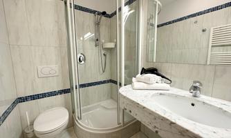 A modern bathroom with a shower, a sink, and bright tiles. Towels are neatly placed on the shelf.