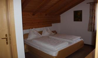 A cozy bedroom with a double bed and wooden ceiling. There are two large pillows and a small table in the room.