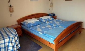 A cozy bedroom with a wooden bed and blue bedding. Next to the bed is a wooden table with a checked tablecloth.