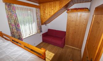 A cozy room with a wooden ceiling and a red sofa. The window has colorful curtains and offers a view outside.