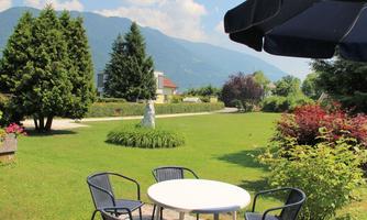 A beautiful garden with a table and chairs. In the background, there are trees and mountains.