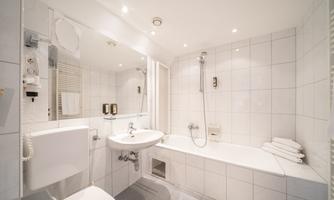 A modern bathroom with white tiles, a bathtub, and a sink. It is well-lit and clean.