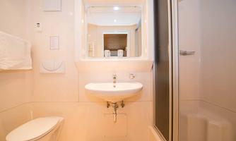 A modern bathroom with a sink, mirror, and shower. The walls are light, and the fixtures are simple and clean.
