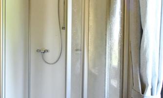 A modern shower cubicle with clear walls and a hand-held showerhead. The space is designed to be light and welcoming.