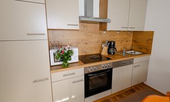 A modern kitchen with wood and white cabinet fronts. It is well equipped with a stove, a coffee machine, and a sink.