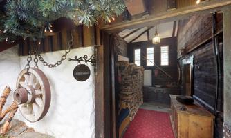 An inviting entrance area with a large wheel and a cozy woodpile. The walls are made of dark wood and the floor is covered with a red carpet.
