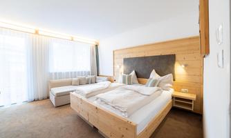 A modern hotel room with two beds and a wood design. The room is bright and cozy, with a sofa and large windows for plenty of light.