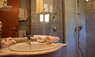 A modern bathroom with a sink, towels, and a shower. The walls are covered with gray tiles.