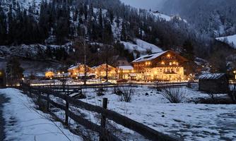 A picturesque village in the snow at dusk. The illuminated houses radiate warm light into the cold winter landscape.