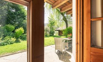 A view of a beautiful garden with green plants and a table with chairs. The sun is shining through the window, creating an inviting atmosphere.