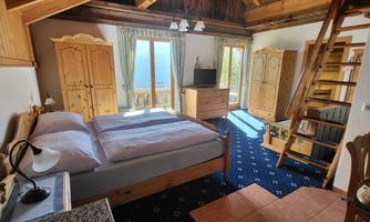 A bright room with wooden decor and a large bed. There are windows with a view outside and a cozy staircase.