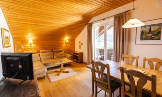 A cozy living room with a wooden ceiling, a lounge area, and a dining area. Large windows let in plenty of light and provide access to a balcony.