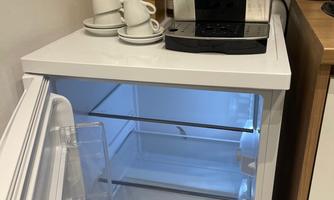 A modern kitchen with a refrigerator and a coffee maker. The refrigerator is open and shows empty shelves.