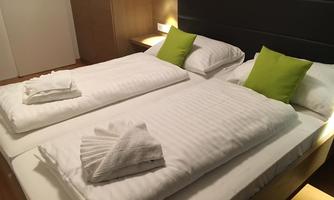 A cozy bedroom with two single beds and fresh white bedding.  
On each bed lies a pillow with a green cover and a towel.