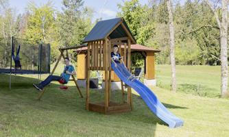 A playground with a slide and a swing, where two children are playing. In the background, there are trees and a peaceful meadow.