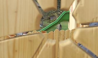 A playground with a green slide is visible through a wooden railing. The slide is part of a child-friendly outdoor area.