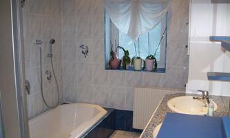 A bathroom with a bathtub and sink. The walls are tiled and there are plants by the window.