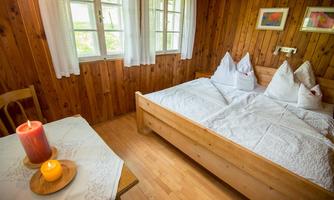A cozy bedroom with wood paneling and a double bed. Candles and a tablecloth are on the table.