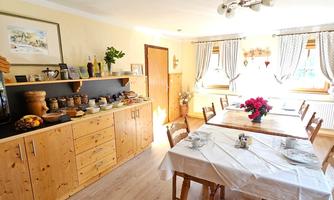 A bright kitchen with wooden furniture and a large dining table. The room is friendly decorated and offers space for several people.