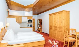 A cozy room with wooden decor and a large bed. There is a small kitchen and a dining table, surrounded by warm colors.