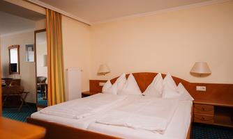 A cozy bedroom with a double bed and several pillows. The walls are beige, and there is warm lighting from the lamps.
