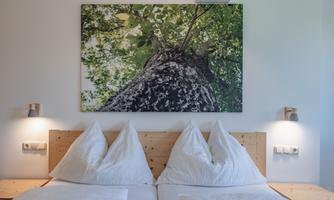A cozy bedroom with a large picture of a tree on the wall. The beds are decorated with white pillows.