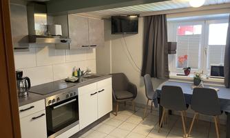 A modern kitchen with a dining area. The amenities include an oven, a refrigerator, and a table with chairs.