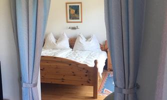 A cozy bedroom with wooden beds and white pillows. The room is visible through an arched entrance and blue curtains.