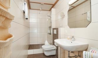 A modern bathroom with a shower, a sink, and a toilet. The walls are brightly tiled, and there are fresh towels and a large mirror.