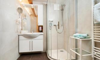 A modern bathroom with a shower and a sink. The walls are light and the furnishings are clean and functional.