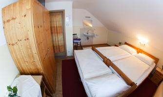 A cozy room with two single beds and a wooden wardrobe. There is a small sink and a pleasant atmosphere.