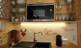 A cozy kitchen corner with a modern microwave, dishes, and glasses on shelves. Decorative greetings in different languages are displayed on the wall.