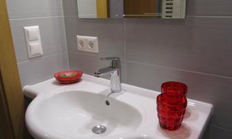 A modern bathroom with an elegant sink and mirror. Red glasses and a bowl provide a colorful accent.