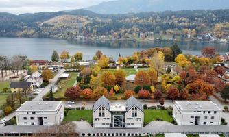 A picturesque view of a residential area with modern buildings and colorful deciduous trees. In the background, a peaceful lake and gentle hills can be seen.