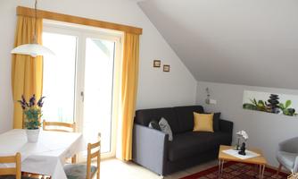 A cozy living space with a gray sofa and a table. Large windows with yellow curtains provide ample light.
