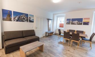 A modern living room with a sofa and a dining table. Pictures of mountains hang on the walls.