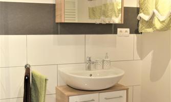 A modern bathroom with a sink and a mirror. The walls are painted in neutral colors, and there are green curtains and towels.