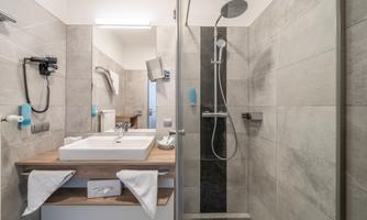 A modern bathroom with a shower and a wooden sink. The walls are in neutral gray tones, and there are fresh towels.