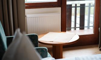 A cozy room with a chair and a table. Through the window, you can see a green landscape by the water.