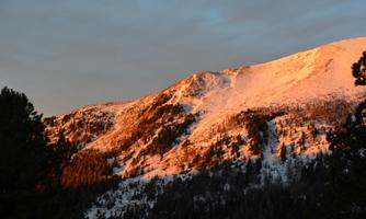 A beautiful mountain with snow-covered slopes illuminated by the evening sun. The sky is clear and has gentle clouds.