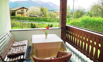 A cozy balcony with a table and chairs. In the background, green meadows and mountains can be seen.