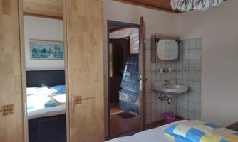 A cozy bedroom with two single beds and a bright atmosphere. In the background, a sink and an open door frame are visible.